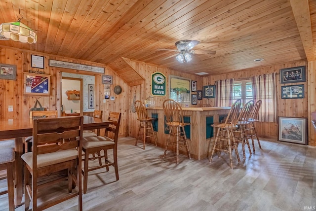 dining area with wood ceiling, indoor bar, light hardwood / wood-style flooring, and wood walls