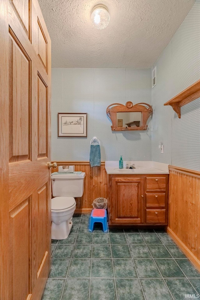 bathroom with vanity, a textured ceiling, wooden walls, and toilet