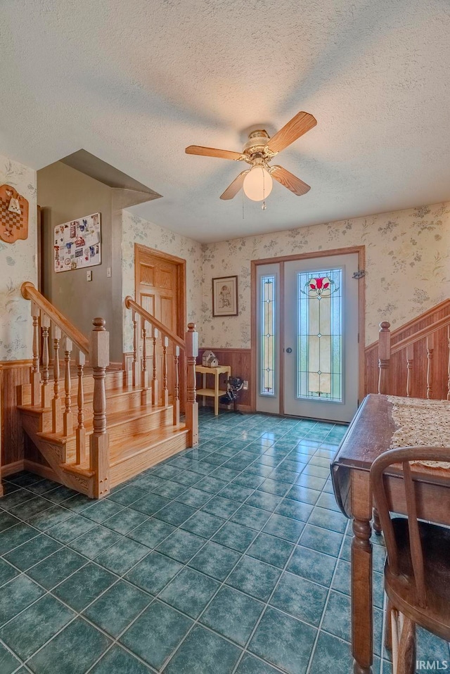 entryway featuring dark tile patterned floors, ceiling fan, wooden walls, and a textured ceiling