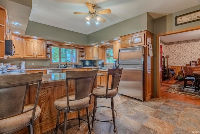 kitchen with ceiling fan, appliances with stainless steel finishes, a kitchen breakfast bar, and sink