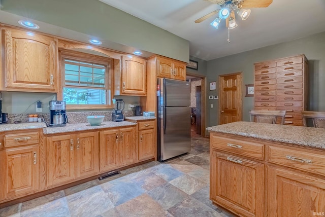 kitchen with stainless steel refrigerator, ceiling fan, and light stone counters