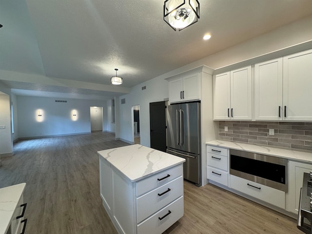 kitchen with tasteful backsplash, white cabinets, light stone counters, stainless steel refrigerator, and light wood-type flooring