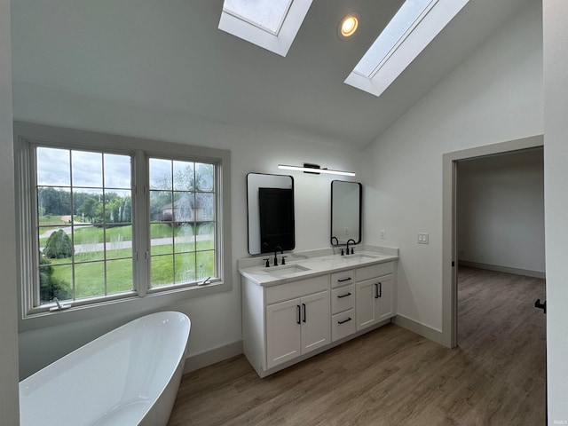 bathroom featuring wood-type flooring, double sink vanity, vaulted ceiling with skylight, and a bathtub