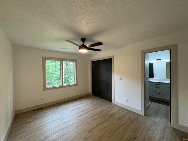 unfurnished bedroom featuring a closet, connected bathroom, light hardwood / wood-style floors, a textured ceiling, and ceiling fan