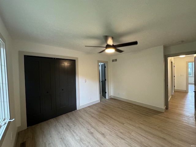 unfurnished bedroom featuring light hardwood / wood-style floors, a closet, a textured ceiling, and ceiling fan