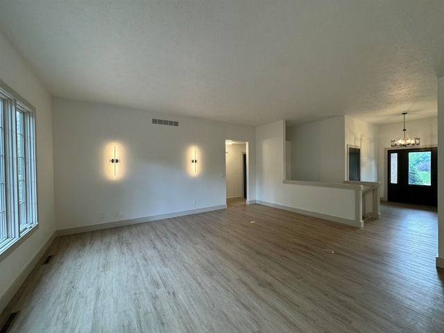 unfurnished living room featuring wood-type flooring, a textured ceiling, and an inviting chandelier