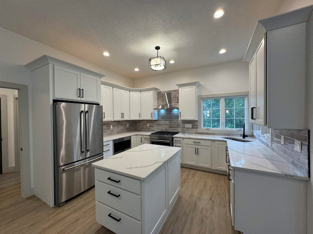 kitchen with appliances with stainless steel finishes, light hardwood / wood-style flooring, tasteful backsplash, sink, and wall chimney exhaust hood