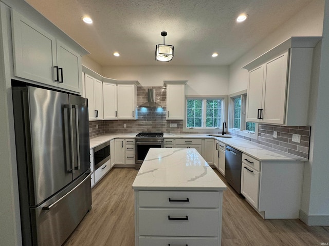 kitchen featuring appliances with stainless steel finishes, backsplash, light wood-type flooring, and wall chimney exhaust hood