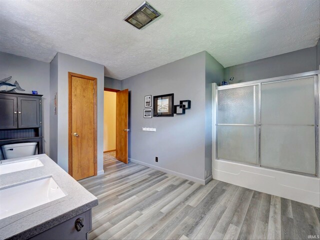 full bathroom featuring toilet, wood-type flooring, a textured ceiling, and bath / shower combo with glass door