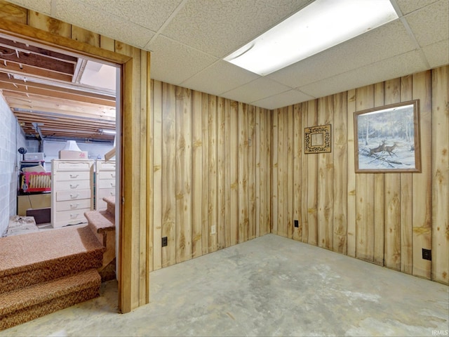 basement featuring wood walls and a drop ceiling