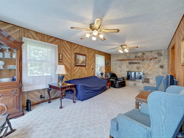 carpeted living room featuring a fireplace, wood walls, a textured ceiling, and ceiling fan