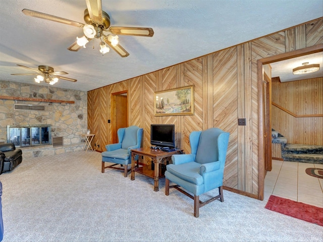 interior space featuring carpet floors, a stone fireplace, wooden walls, and ceiling fan