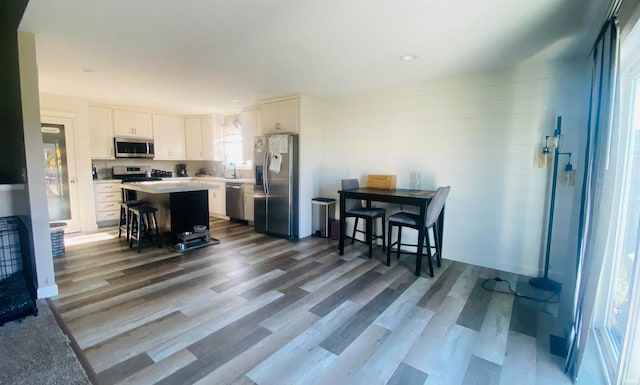 kitchen featuring appliances with stainless steel finishes, a breakfast bar area, wood-type flooring, a kitchen island, and white cabinetry