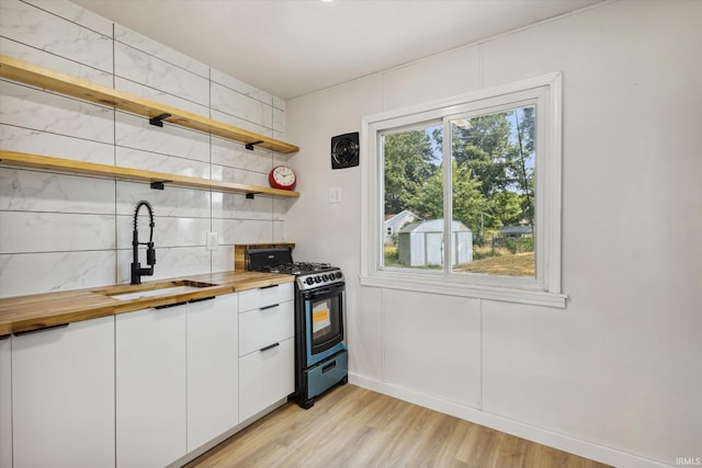 kitchen with white cabinets, sink, butcher block counters, light wood-type flooring, and black range with gas stovetop