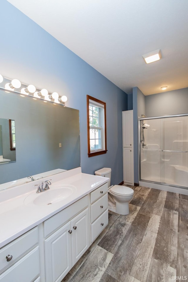 bathroom featuring a shower with door, vanity, wood-type flooring, and toilet