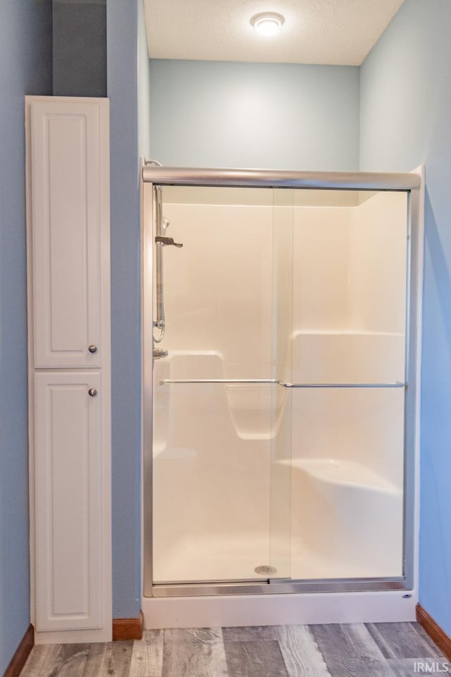 bathroom with wood-type flooring, a textured ceiling, and a shower with shower door