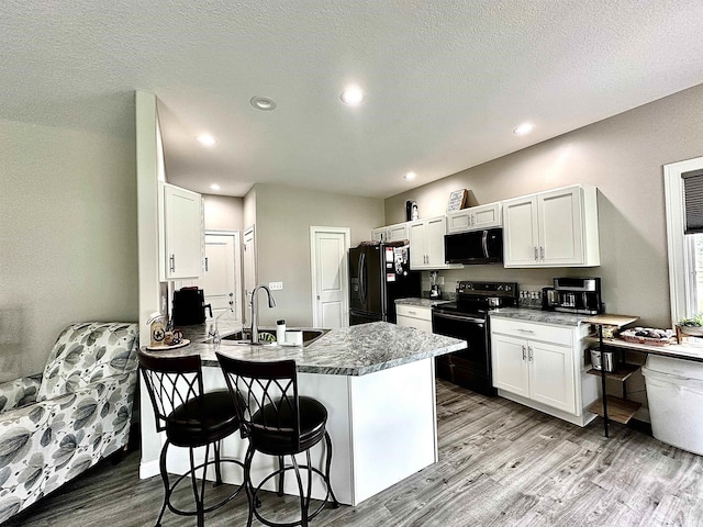 kitchen with sink, white cabinets, a kitchen breakfast bar, black appliances, and light hardwood / wood-style flooring