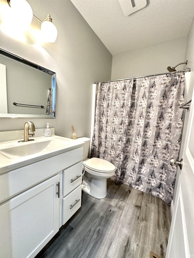 bathroom featuring curtained shower, hardwood / wood-style floors, vanity, toilet, and a textured ceiling