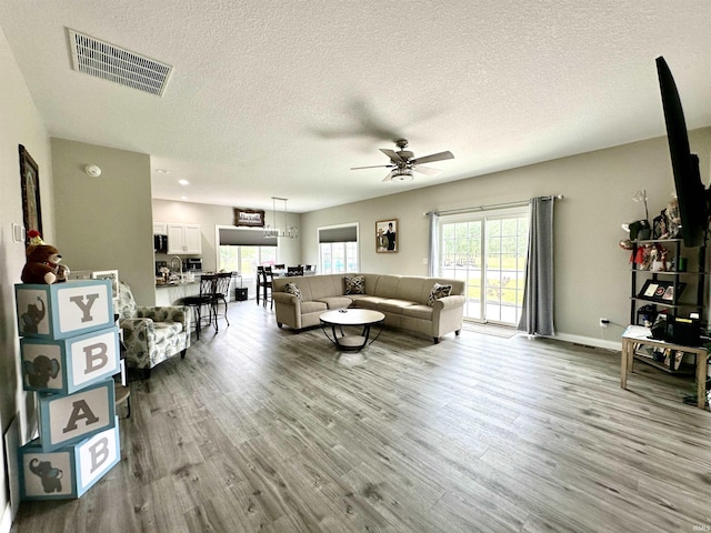 living room featuring ceiling fan, a textured ceiling, and light hardwood / wood-style flooring