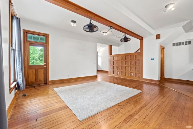 unfurnished living room featuring light wood finished floors, beamed ceiling, visible vents, and baseboards