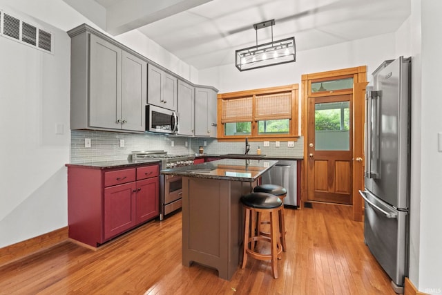 kitchen featuring tasteful backsplash, visible vents, appliances with stainless steel finishes, light wood-type flooring, and a kitchen bar