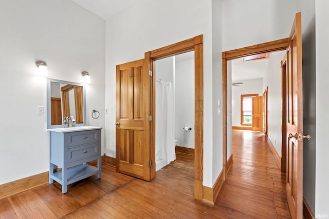 hallway with light wood finished floors, a sink, a towering ceiling, and baseboards