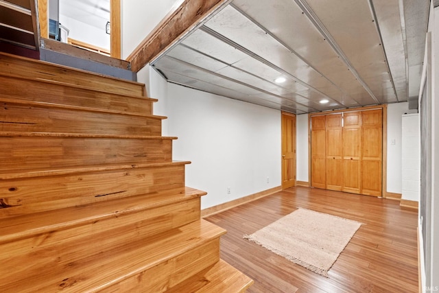 finished below grade area featuring stairs, light wood finished floors, and baseboards