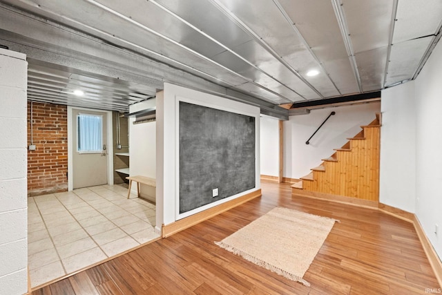 finished basement featuring brick wall, stairs, baseboards, and wood finished floors