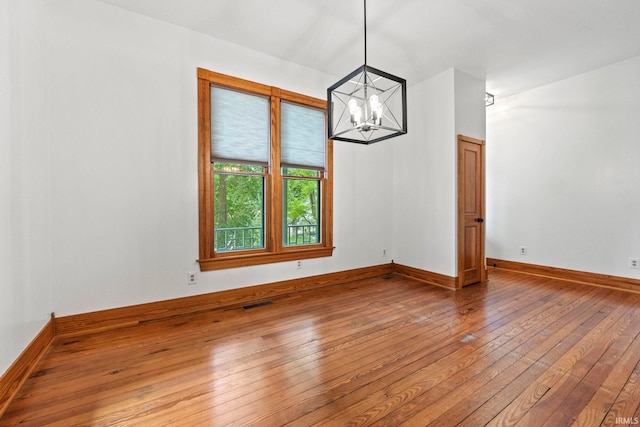 spare room with visible vents, a chandelier, hardwood / wood-style flooring, and baseboards