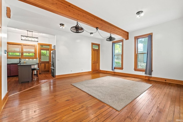 unfurnished living room featuring beam ceiling, a sink, baseboards, and hardwood / wood-style flooring