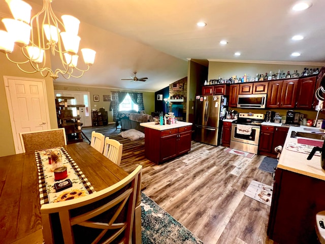 kitchen with vaulted ceiling, light wood-type flooring, stainless steel appliances, and decorative light fixtures