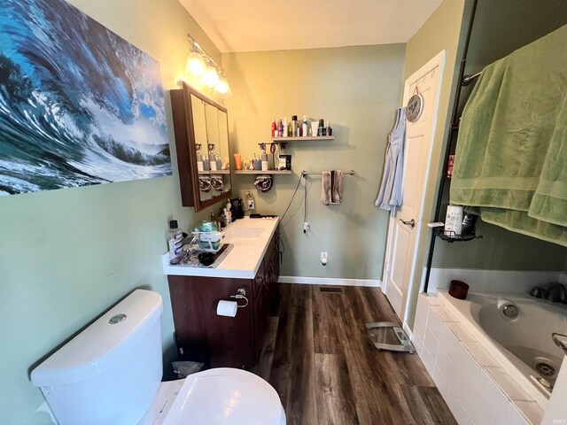 bathroom featuring baseboards, tiled tub, toilet, wood finished floors, and vanity