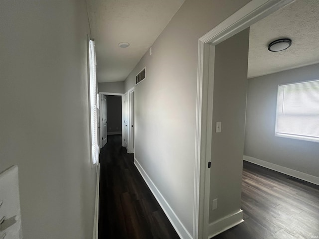 corridor featuring visible vents, baseboards, dark wood finished floors, and a textured ceiling