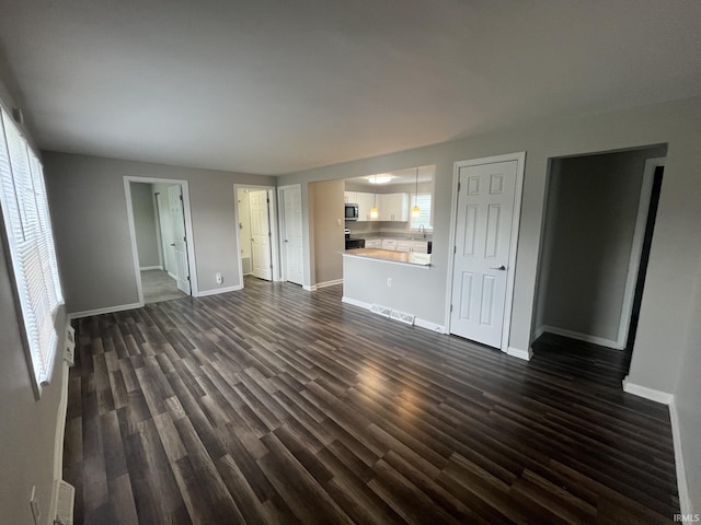 unfurnished living room featuring a sink, baseboards, visible vents, and dark wood-style flooring