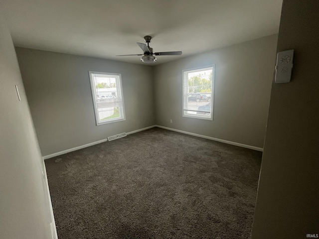 unfurnished room featuring a wealth of natural light, dark carpet, and visible vents