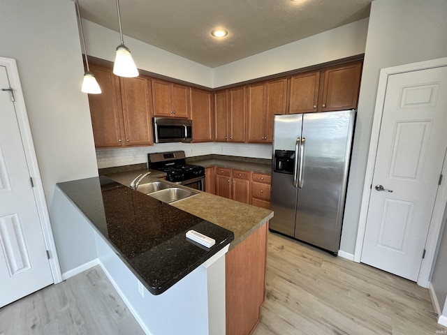 kitchen featuring decorative light fixtures, sink, kitchen peninsula, stainless steel appliances, and light hardwood / wood-style flooring