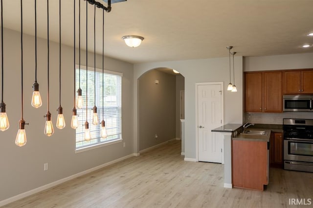 kitchen with sink, light hardwood / wood-style flooring, appliances with stainless steel finishes, hanging light fixtures, and decorative backsplash