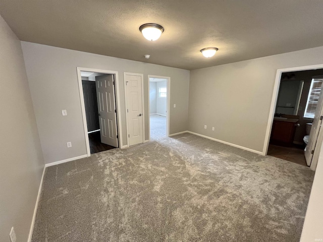 unfurnished bedroom with ensuite bathroom, a textured ceiling, and dark colored carpet