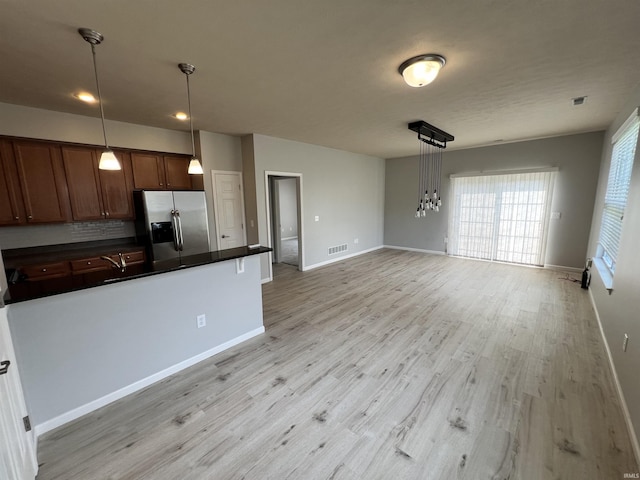 kitchen with pendant lighting, tasteful backsplash, light hardwood / wood-style floors, and stainless steel refrigerator with ice dispenser