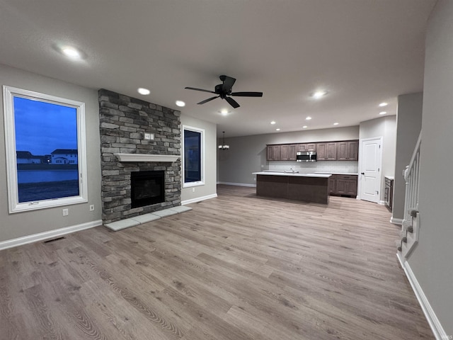 unfurnished living room with a stone fireplace, ceiling fan, and light hardwood / wood-style flooring