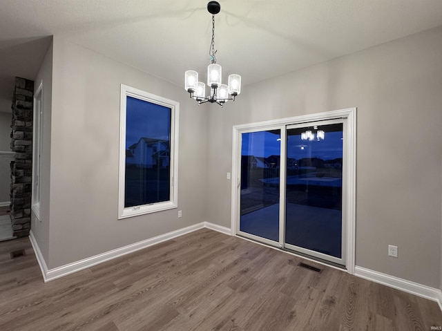 unfurnished dining area with hardwood / wood-style floors and a notable chandelier