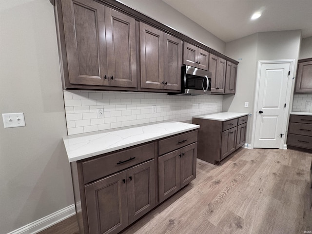 kitchen with dark brown cabinetry, decorative backsplash, light stone countertops, and light wood-type flooring