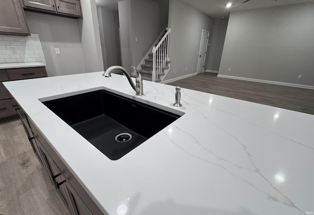 kitchen with decorative backsplash, light hardwood / wood-style floors, light stone countertops, and sink