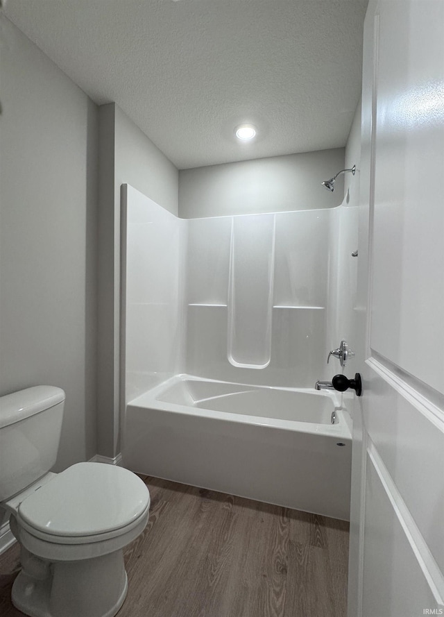 bathroom with washtub / shower combination, wood-type flooring, a textured ceiling, and toilet