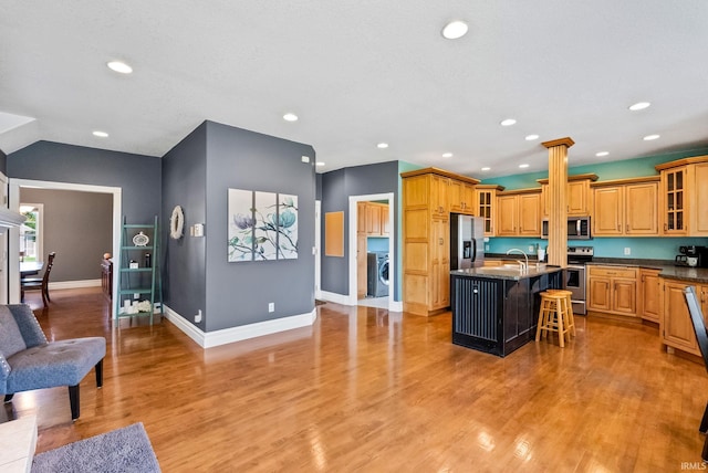 kitchen with a breakfast bar, light hardwood / wood-style flooring, washer / clothes dryer, an island with sink, and stainless steel appliances