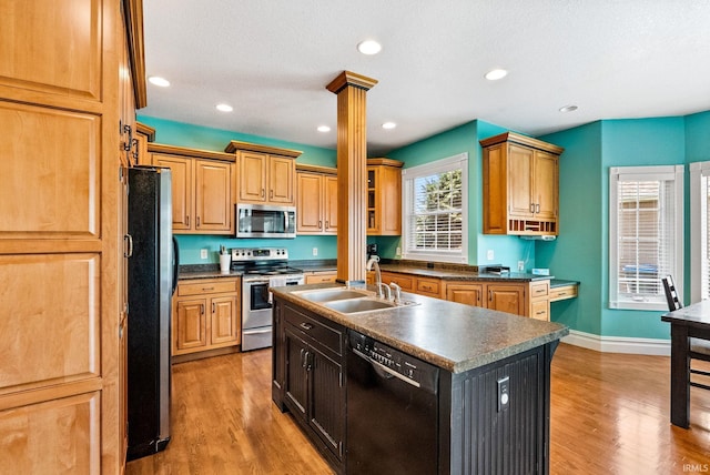 kitchen with decorative columns, light wood-type flooring, stainless steel appliances, sink, and a center island with sink