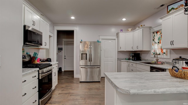 kitchen with white cabinets, sink, kitchen peninsula, appliances with stainless steel finishes, and light hardwood / wood-style floors