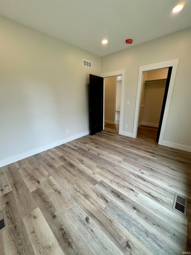 unfurnished bedroom featuring light wood-type flooring, a walk in closet, and a closet