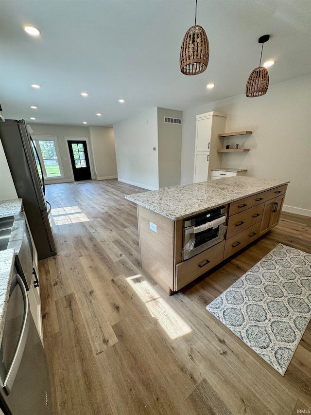 kitchen featuring hanging light fixtures, light wood-type flooring, light stone countertops, stainless steel appliances, and a kitchen island