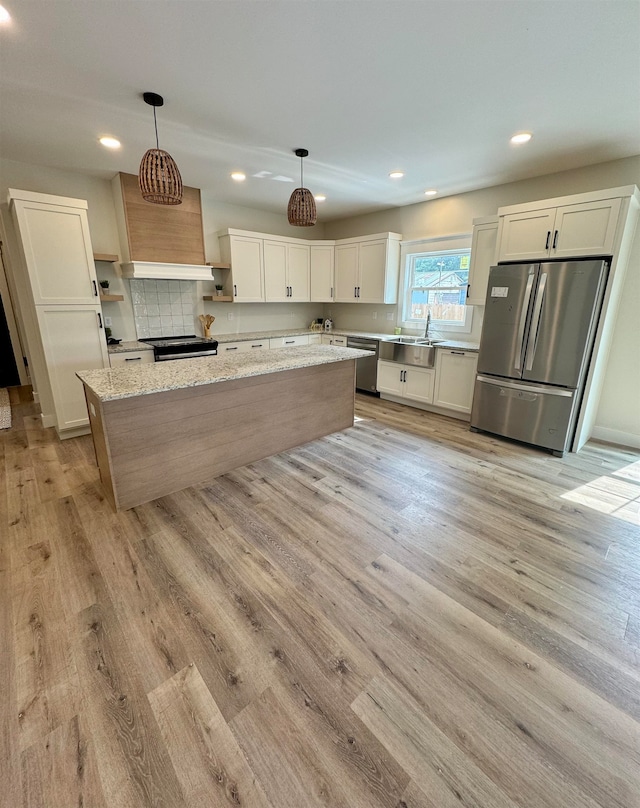 kitchen with hanging light fixtures, a center island, light wood-type flooring, appliances with stainless steel finishes, and light stone countertops